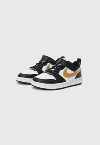 Atletske cipele u crnoj, bijeloj i zlatnoj boji s kožnim gornjim dijelom, perforiranim prstom, čičak trakama i gumenim potplatom. Sadrži Nike logo u zlatnoj boji.