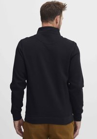 Fekete pulóver magas gallérral, textúrált anyagból, hosszú ujjakkal. A háta varrás nélküli dizájnnal és laza szabással rendelkezik.