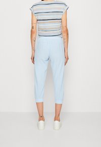 Lichtblauwe, cropped broek met elastische tailleband en opgerolde zoom, gecombineerd met een gestreept T-shirt met korte mouwen in pastelkleuren. Witte sneakers.