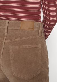 Bruna kordflossbyxor med en strukturerad yta, som har en bakficka och en läderlapp märkt 'Madewell' nära midjan.