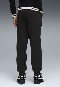 Pantalons de survêtement noirs avec une coupe décontractée, dotés d'une poche latérale et de poignets côtelés, assortis à des baskets noires avec des accents blancs.