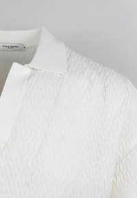 Polo shirt bianco lavorato a maglia con un motivo testurizzato, maniche corte e un colletto classico piatto. L'etichetta riporta "PAOLO PECORA MILANO."