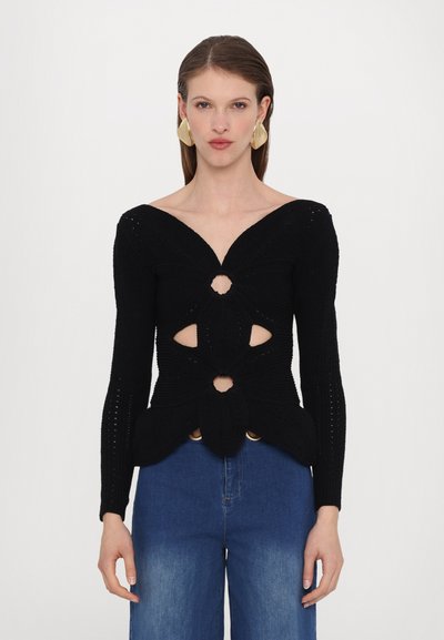 Pull en tricot noir avec un décolleté en V profond, des découpes, et des manches longues, associé à un jean en denim bleu taille haute.