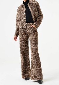 Jasped jacka och utsvängda byxor i brunt och creamfärgad tyg. Knappar på jackan, svart topp under, och eleganta svarta skor.