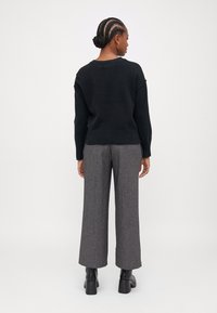 Pulôver preto tricotado com decote redondo, combinado com calças largas cinza xadrez e botins pretos de salto bloco.