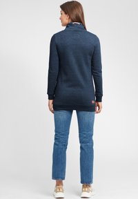 Mörkblå tröja med hög krage, långa ärmar och rundad nederkant. Tillverkad av mjukt material, med en logotypdetalj vid kragen. Buren med denimjeans.