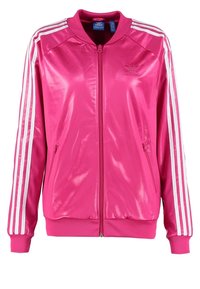 Rosa satinjacka med dragkedja och vita tre-rands detaljer på ärmarna, ribbad mudd och nederkant, samt en liten logotyp på bröstet.