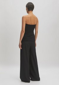 Schwarzes trägerloses Oberteil kombiniert mit weiten schwarzen Hosen. Glattes Material, taillierter Oberteil und ein sauberes, minimalistisches Design ohne Muster.