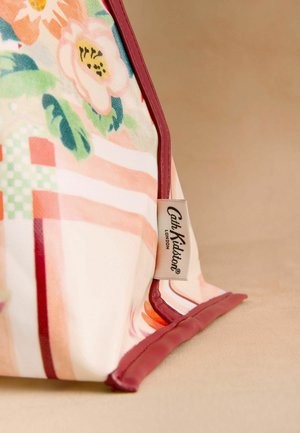 Hjørne af blomsterprintet stof med bordeaux kant og Cath Kidston London mærke på beige overflade.