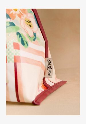 Róg tkaniny w kwiatowy wzór z bordowym obszyciem i metką marki Cath Kidston London na beżowej powierzchni.