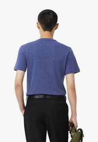 T-paita lyhythihaisena, pyöreällä kauluksella harmaansinisessä kankaassa, tekstuuri viimeistelyllä. Yhdistetty mustiin housuihin ja pidetään vihreää laukkua.