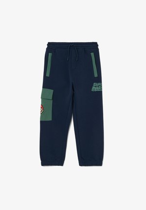 Pantalones jogger azul marino con detalles de bolsillo verdes, cinturilla y puños elásticos, logo de Super Mario en el muslo y parche del personaje Mario en el bolsillo lateral.