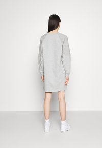 Robe pull grise avec texture matelassée sur les manches, poignets côtelés, coupe décontractée et longueur genou. Portée avec des baskets blanches.