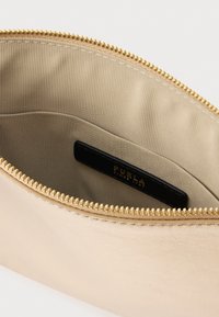 Zelta metālisks maciņš ar gludu ārpusi, rāvējslēdzēja aizdari un gaiši brūnu oderi ar melnu zīmola birku.