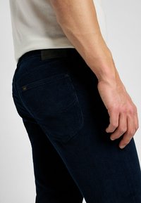 Jeans in corduroy di colore navy con una vestibilità aderente, dotati di tasche posteriori e un'etichetta in pelle sulla vita. Superficie testurizzata con righe.