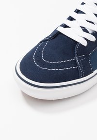 Světlomodrý semišový tenisky s bílým prošíváním, bílou gumovou podrážkou a bílými šňůrkami; má perforace pro ventilaci a designové akcenty.