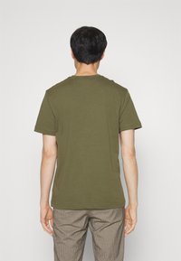 Tricou verde cu mânecă scurtă, fabricat din bumbac moale, având guler rotund și o croială lejeră, asortat cu pantaloni cu model în carouri.