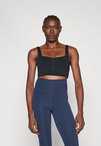 Μαύρο αθλητικό τοπ με τετράγωνη λαιμόκοψη και χοντρές τιράντες, συνδυασμένο με ψηλόμεσα σκούρα μπλε κολάν με λεία υφή.