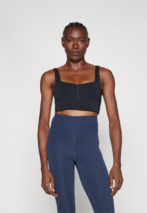 Crni sportski crop top sa četvrtastim izrezom i debelim trakama, uparen s tajicama tamnoplave boje visokog struka koje imaju glatku teksturu.