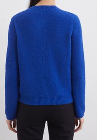 Pletený modrý svetr s texturovaným, hebkým povrchem. Obsahuje kulatý výstřih, dlouhé rukávy a vroubkovaný lem, navržený pro volný střih.