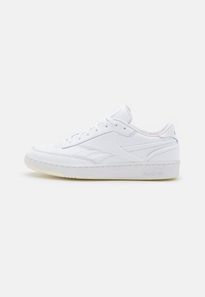 Hvid lavtopet lædersneaker med snørelukning og tekstureret sål, med subtile mærkedetaljer på siden og hælen.