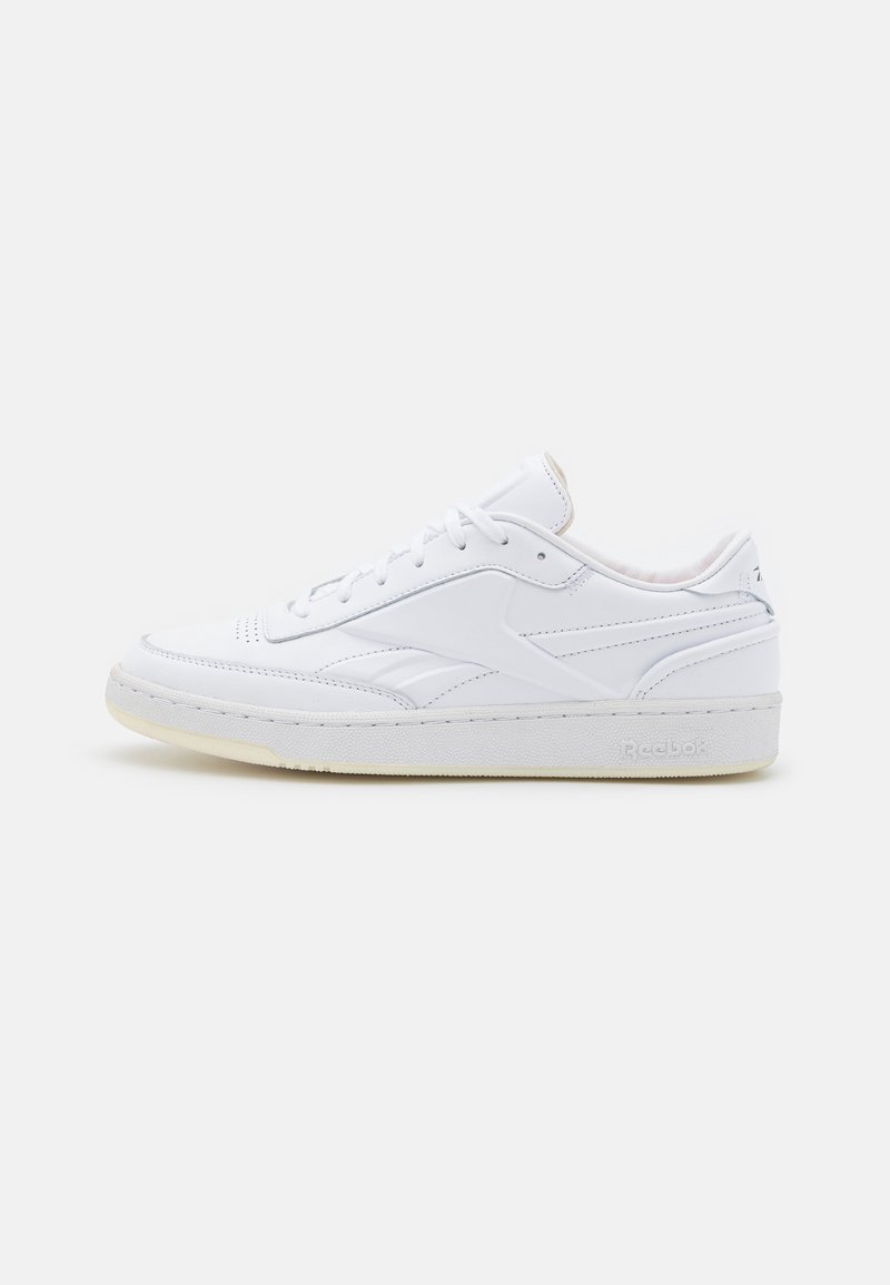 Baskets basses blanches en cuir avec fermeture à lacets et semelle texturée, ornées de détails subtils de la marque sur le côté et le talon.