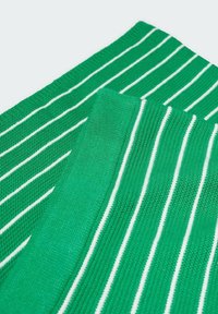 Tissu en maille verte avec de fines rayures blanches verticales, plié pour montrer les détails de la texture et du motif.