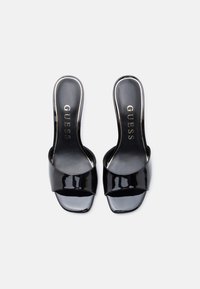 Mule in vernice nera con punta aperta, fascia larga e design slingback. Presenta una finitura lucida e il logo dorato sulla soletta.