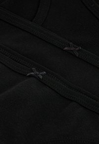 Zwarte stof met ribbelstructuur, voorzien van twee kleine zwarte strikjes aan de bovenkant en platte naden voor comfort. Detailgerichte ontwerp.