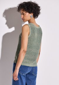 Haut en tricot sans manches vert avec une finition texturée, encolure arrondie et ourlet côtelé. Associé à un jean en denim bleu ample.