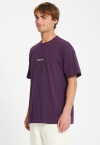 Lilla bomulds t-shirt med rund halsudskæring, korte ærmer og et hvidt "VOLCOM" logo centralt på brystet. Blød, afslappet pasform.