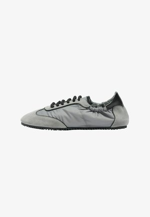 Zapatilla de perfil bajo en gris y negro con detalles de ante, cordones negros, talón elástico y suela estriada, mostrada de perfil.