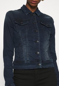 Tmavě modrá džínová bunda s knoflíkovým zapínáním, dvěma náprsními kapsami a klasickým límcem. Nabízí mírně vybledlou texturu a přiléhavý střih.