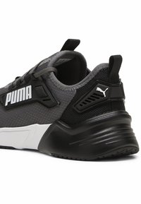 Zapatilla deportiva en negro y gris con parte superior de malla, suela acolchada y logo blanco en el lateral. Presenta un talón texturizado y una lengüeta trasera.