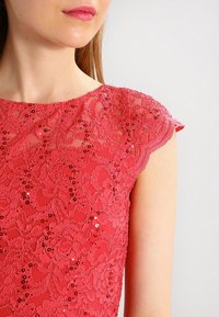 Robe en dentelle rouge avec un motif floral, ornée de sequins et de manches courtes. Texture lisse avec une silhouette ajustée.