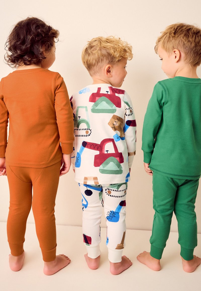 Trois tout-petits pieds nus sont alignés, face à l'arrière, portant des pyjamas à manches longues unis et à motifs sur un fond uni.