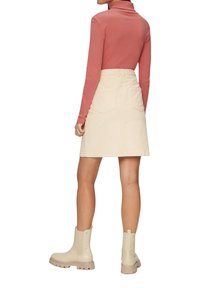 Crème denim rok met twee achterzakken, gecombineerd met een roze longsleeve en beige enkellaarzen. Gladde textuur en getailleerde pasvorm.