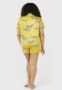 Gult pyjamasæt med et mønster af sort-hvide zebraer. Kortærmet bluse og shorts med afsluttede kanter. Glat stoftekstur.