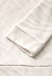 Primo piano della manica di un maglione off-white, caratterizzato da un motivo di maglia testurizzata con linee diagonali e un polsino a costine. Tessuto morbido e leggero.