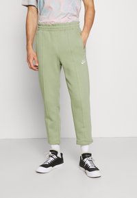 Ljusgröna träningsbyxor med elastisk midja, sidofickor och vit Nike-logga, matchat med svartvita sneakers och vita strumpor.