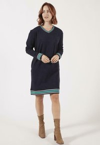 Robe longue à manches longues de couleur marine avec un décolleté en V et des poignets et un ourlet rayés teal contrastants. Tissu doux avec une coupe décontractée. Pas de motifs ni de graphiques visibles.