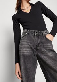 Svart långärmad topp med V-ringning i halsen, kombinerad med högmidjade, blekta svarta jeans. Outfiten kompletteras med ett kedjehalsband.