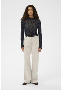 Zwarte lange mouwen top met een textuur van bloemmotieven, gecombineerd met crèmekleurige hoge taille wijde broek en bruine schoenen.