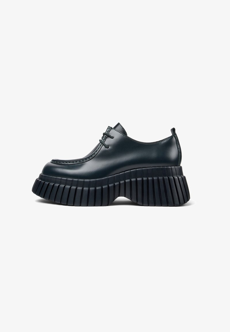 Chaussure plateforme en cuir noir avec semelle épaisse striée, bout arrondi lisse et lacets à l'avant, vue latérale sur fond blanc.