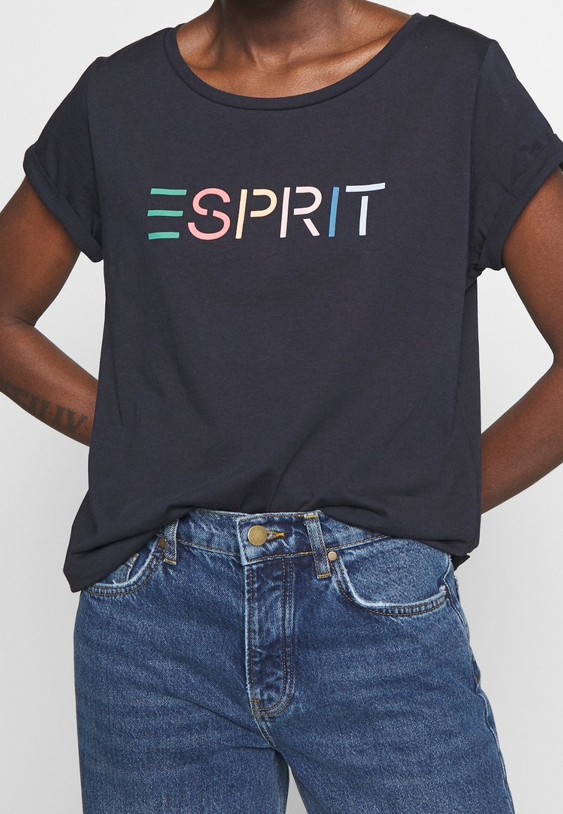 Camiseta de manga corta azul marino con cuello redondo, que presenta el logo "ESPRIT" en múltiples colores en el pecho. Tejido de algodón suave.