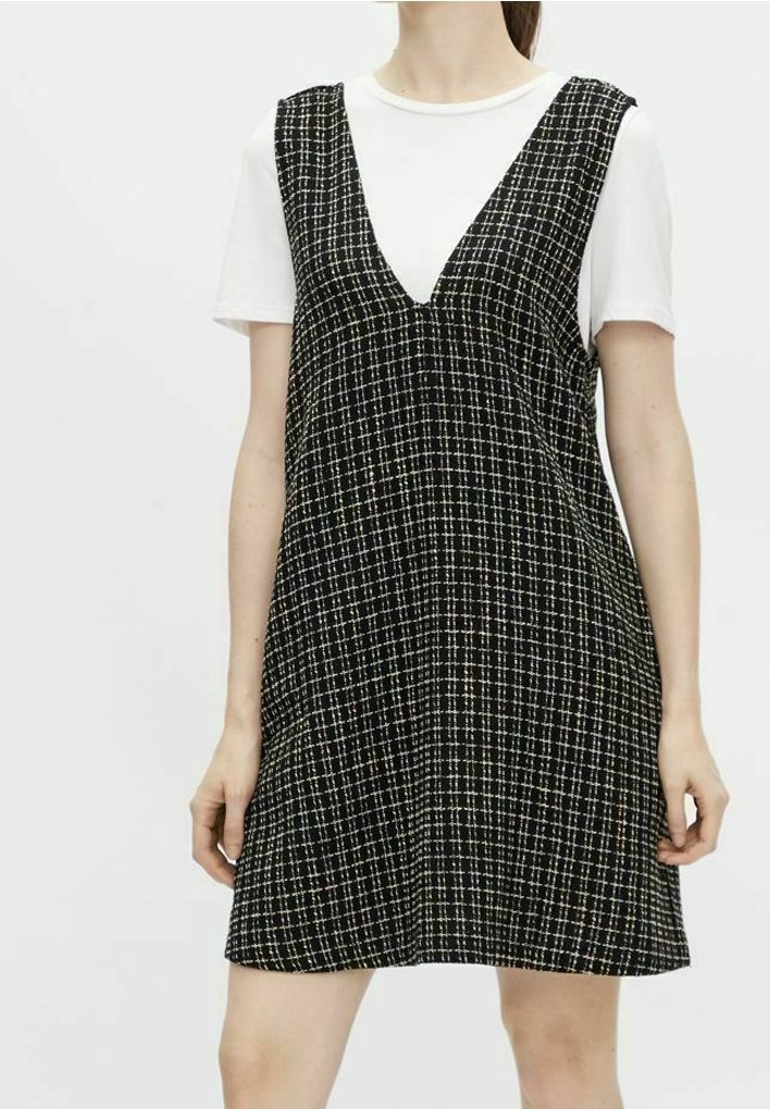 Zwart-wit geruit jurk met een V-hals, met een losse pasvorm en mouwloos ontwerp, over een wit T-shirt.