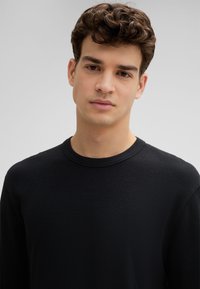Schwarzes Langarmshirt aus strukturiertem Stoff, mit Rundhalsausschnitt und lockerer Passform. Glatte Nähte ohne zusätzliche Verzierungen.