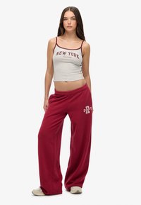 Grijze cropped tanktop met de tekst "NEW YORK", gecombineerd met losse bordeauxrode sjaals met een logo. Casual, zachte stof en een ontspannen pasvorm.