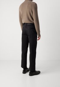 Ljust brunt stickat polotröja i kombination med svarta byxor och svarta skor, som visar en ren design och en strukturerad passform.