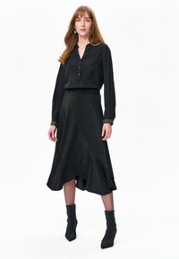 Czarna bluzka z kołnierzykiem i zapięciem na guziki, zestawiona z czarną, błyszczącą spódnicą do kolan. Całość dopełniają czarne, sięgające kostek botki.